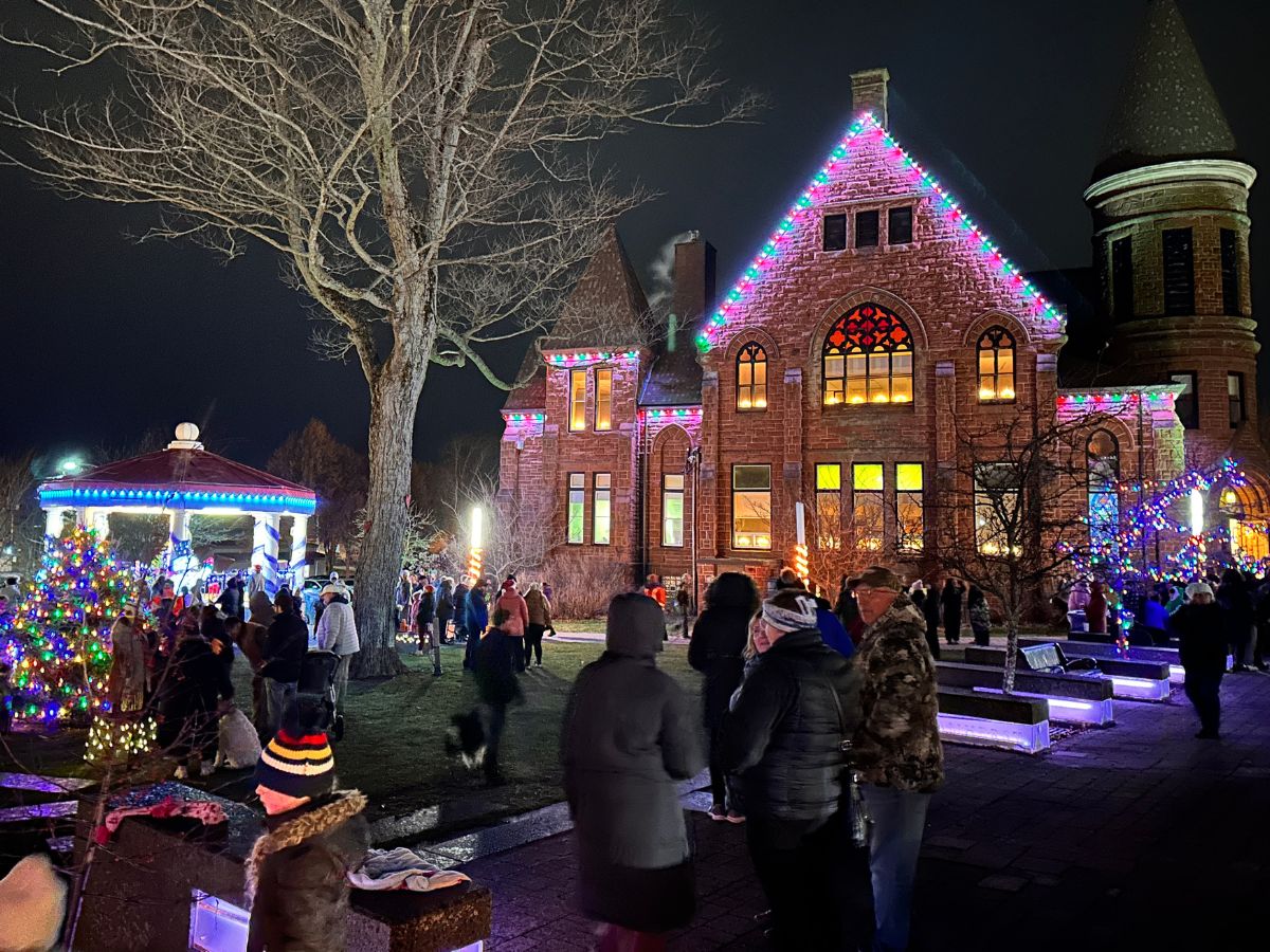 Victoria Square at night with dozens of people admiring the holiday lights on First Baptist Church, the bandstand, and trees in the park